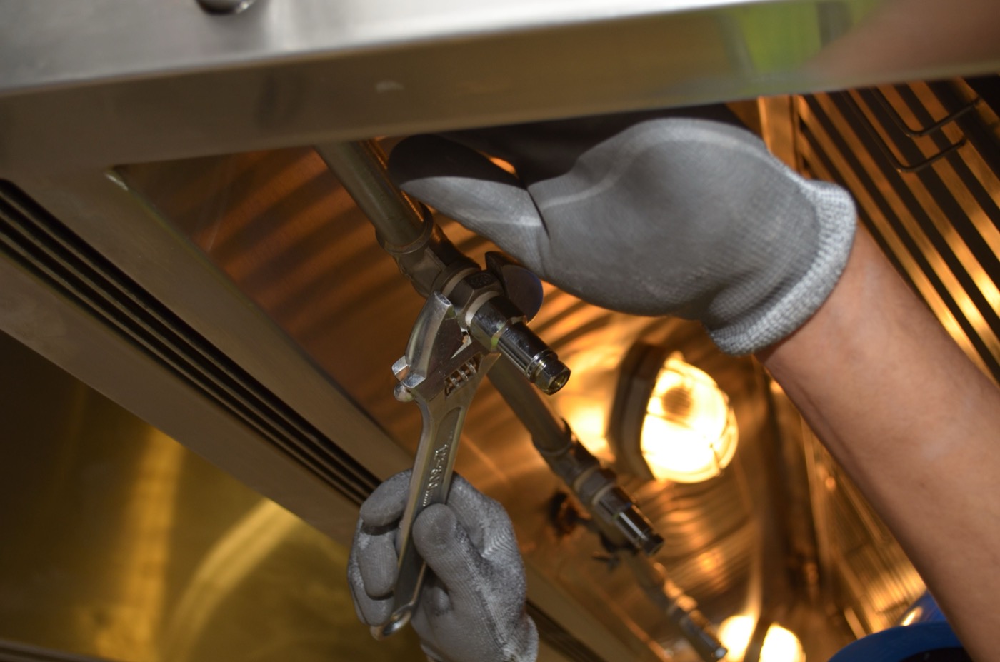 Plumber's gloved hands tightening a pipe fitting with a wrench