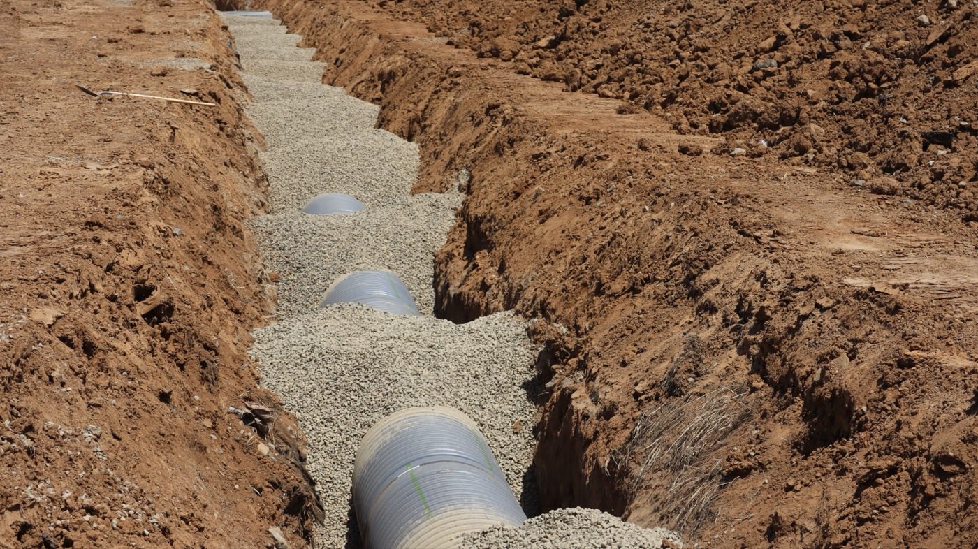 Open trench with a new drainage pipe being laid in gravel